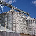 Silos industriais de armazenamento de grãos em uma área agrícola sob céu azul.