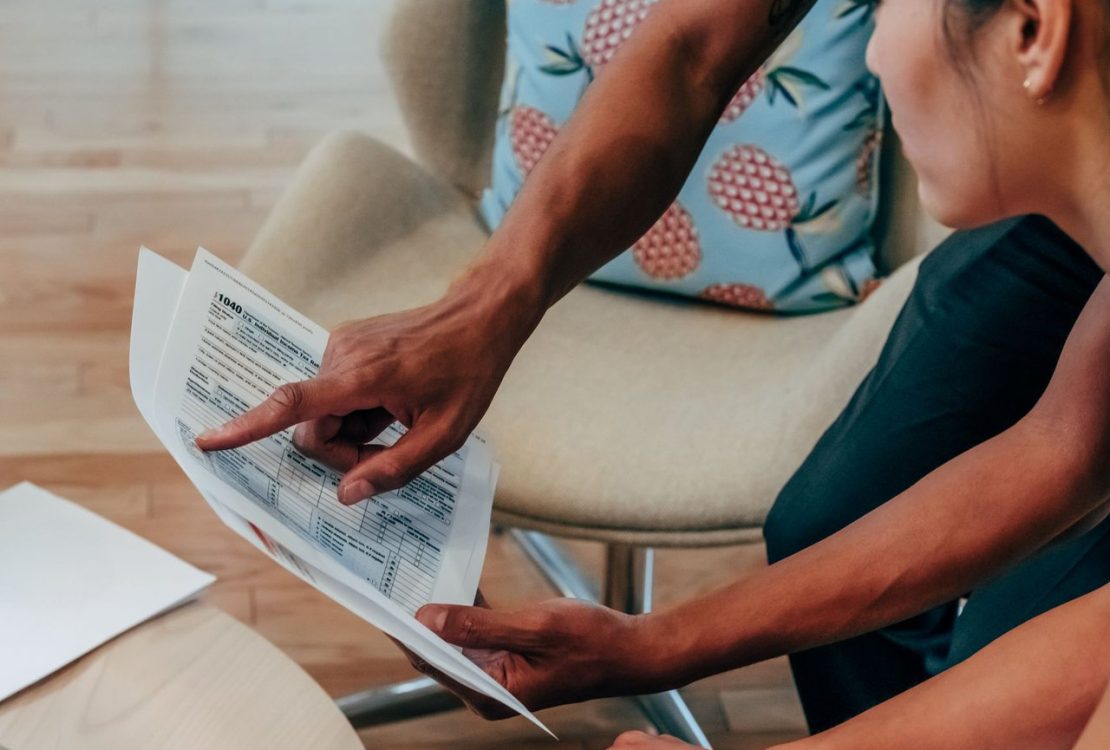Duas pessoas analisam documentos financeiros em um ambiente de trabalho.